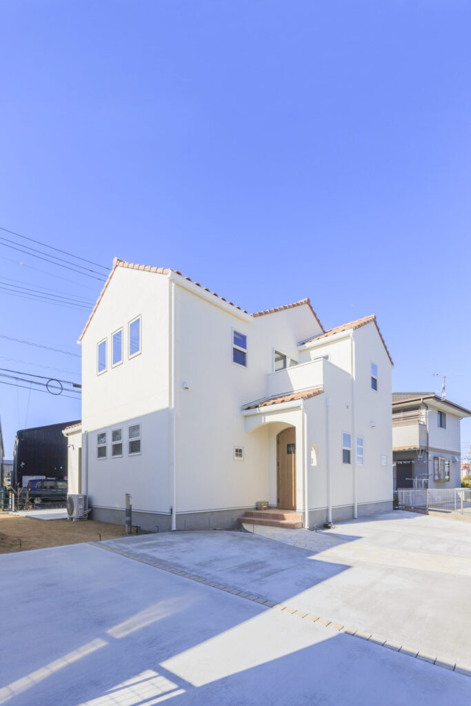 絵本から飛び出したような三角屋根が目を引くプロバンススタイルの外観デザインと道路から玄関が見えないように工夫された設計が組み合わされた注文住宅の外観デザイン